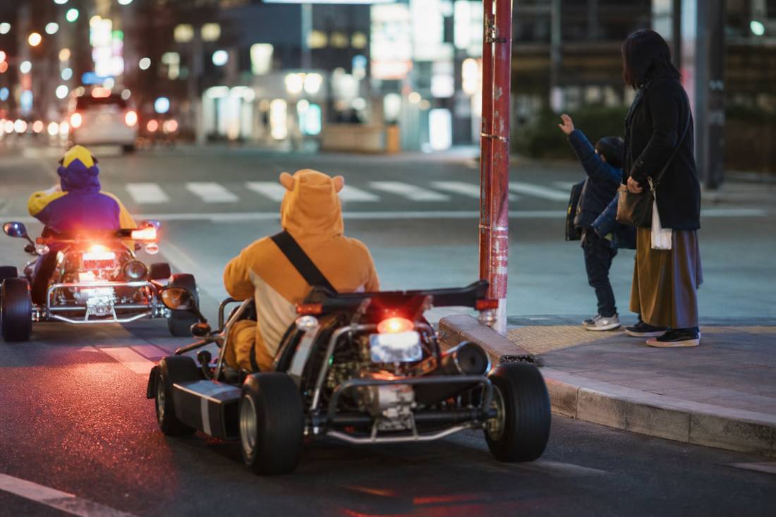 Des parents en kart saluant un enfant sur le trottoir à Tokyo