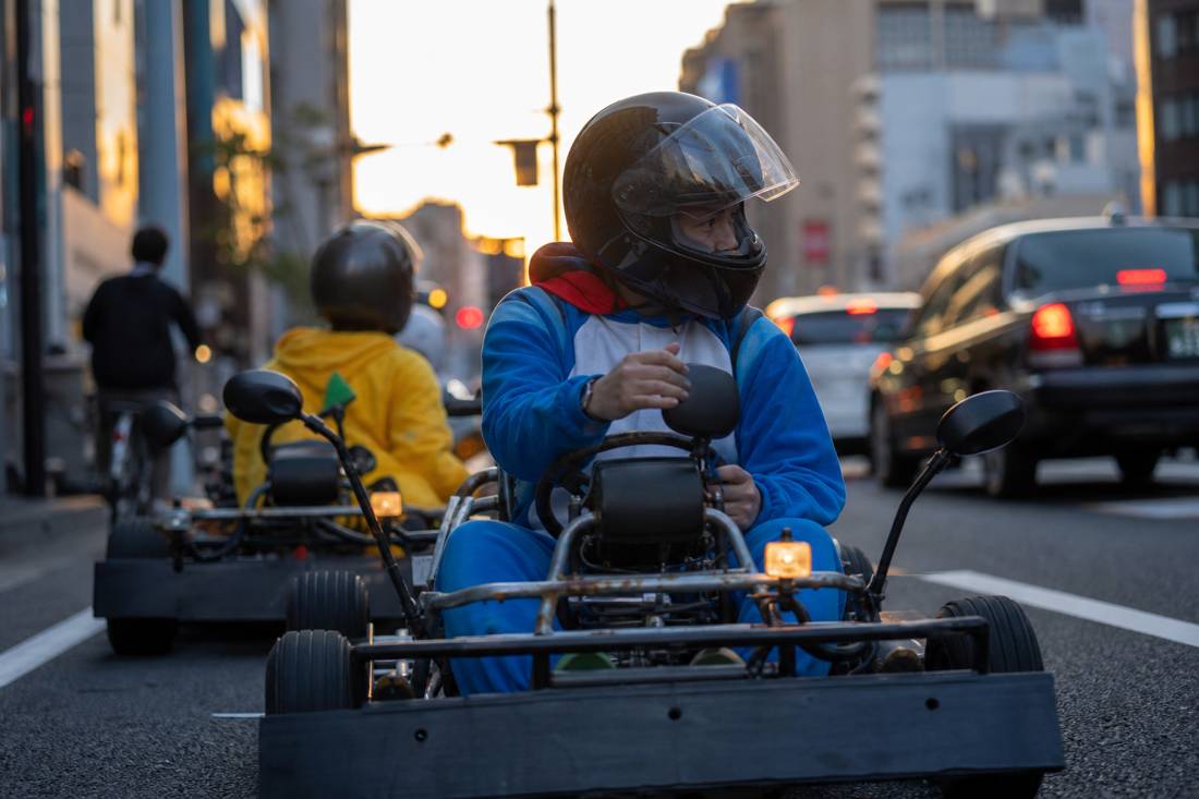東京の交通の中でミラーを確認するヘルメット姿のゴーカートドライバー