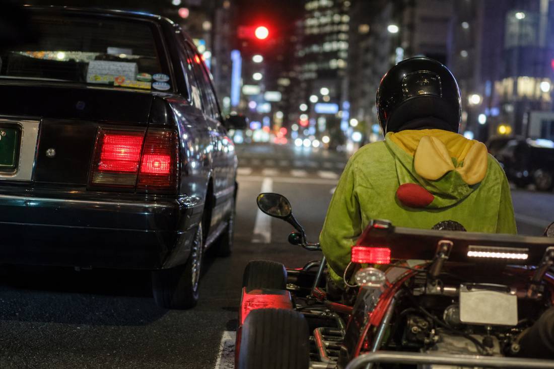 Un go-kart all'altezza degli occhi accanto a un taxi di Tokyo a un semaforo rosso