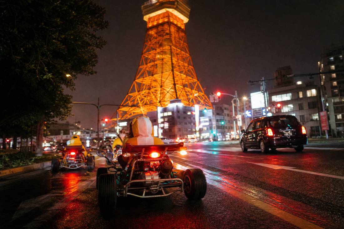 Un go-kart da strada che passa sotto la Tokyo Tower di notte
